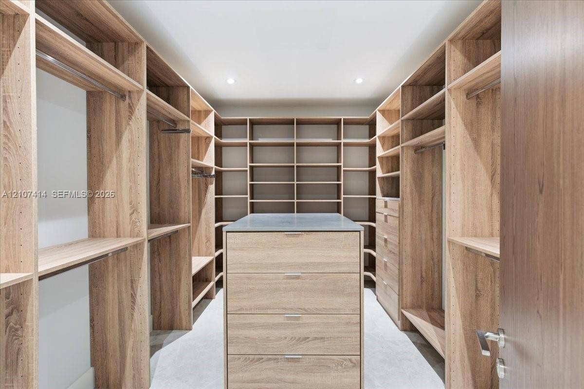 Custom walk-in closet featuring extensive wood-finish built-in shelving, hanging rods, an integrated center island with drawers, and a solid countertop surface