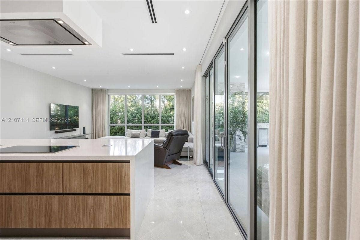 Open-concept kitchen featuring an island with a white countertop and wood-finish cabinetry, floor-to-ceiling glass sliding doors, recessed ceiling lighting, and tile flooring