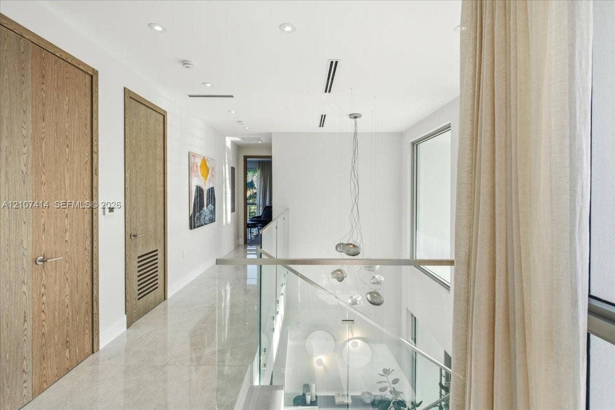 Hallway featuring large-format light tile flooring, wood-finish interior doors, recessed lighting, and a glass panel railing