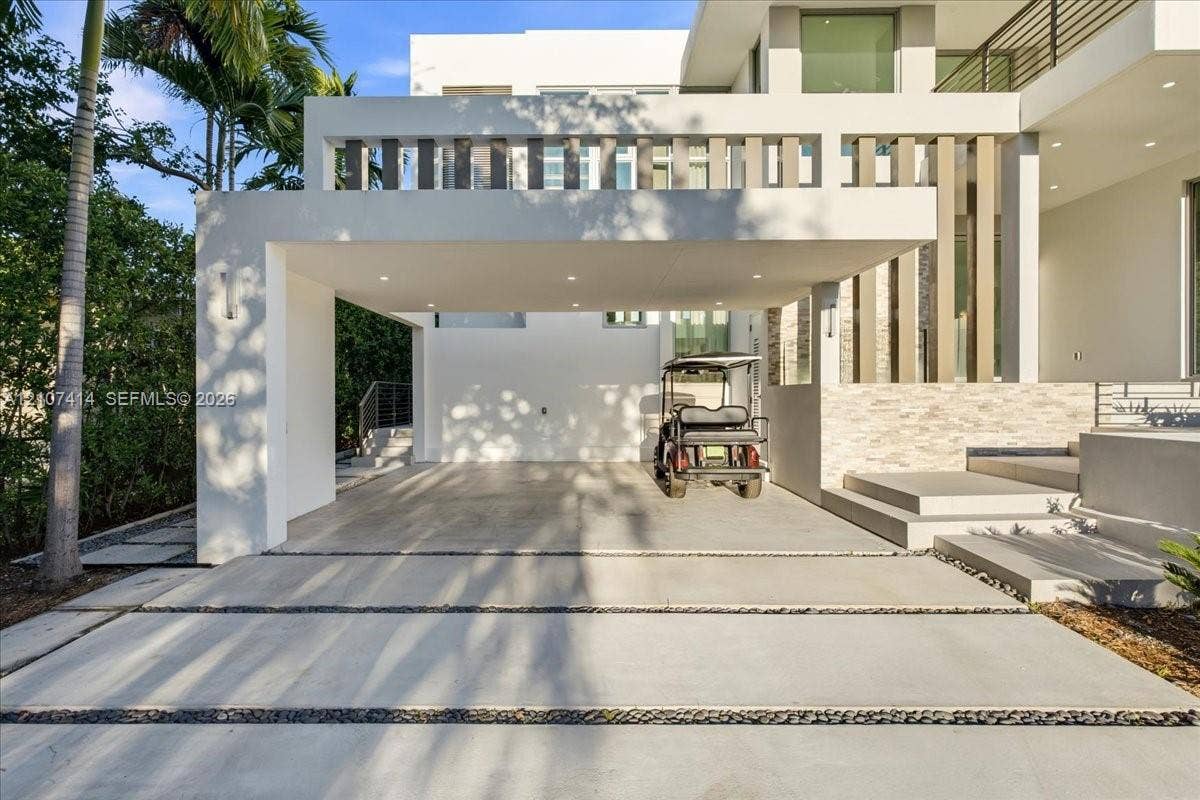 Modern exterior featuring a covered carport, recessed lighting, stone veneer accents, tiered concrete steps, and a segmented concrete driveway with stone inlay