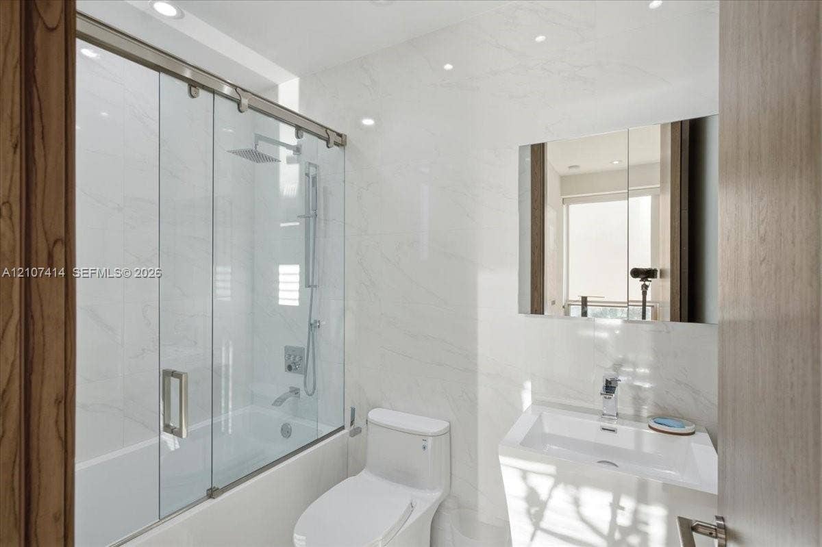 Bathroom featuring full-height stone-finish wall tile, a glass-enclosed shower with a rainfall showerhead, a wall-mounted medicine cabinet, and a contemporary pedestal sink with a chrome faucet