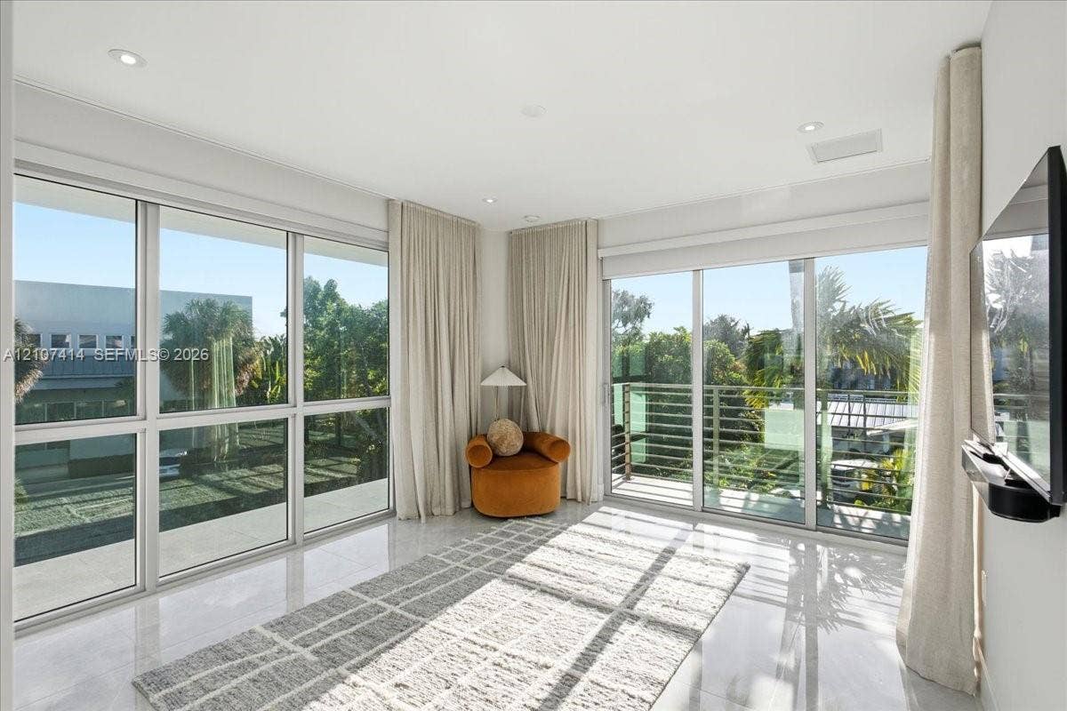 Floor-to-ceiling glass windows, recessed ceiling lighting, light-toned tile flooring, and a private balcony with metal railing