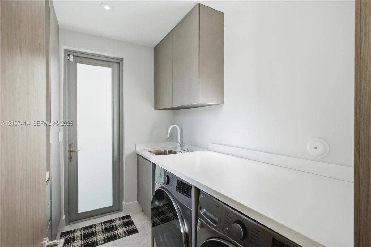 Utility room featuring custom cabinetry, a solid surface countertop, an undermount sink with a high-arch faucet, and a glass-panel door