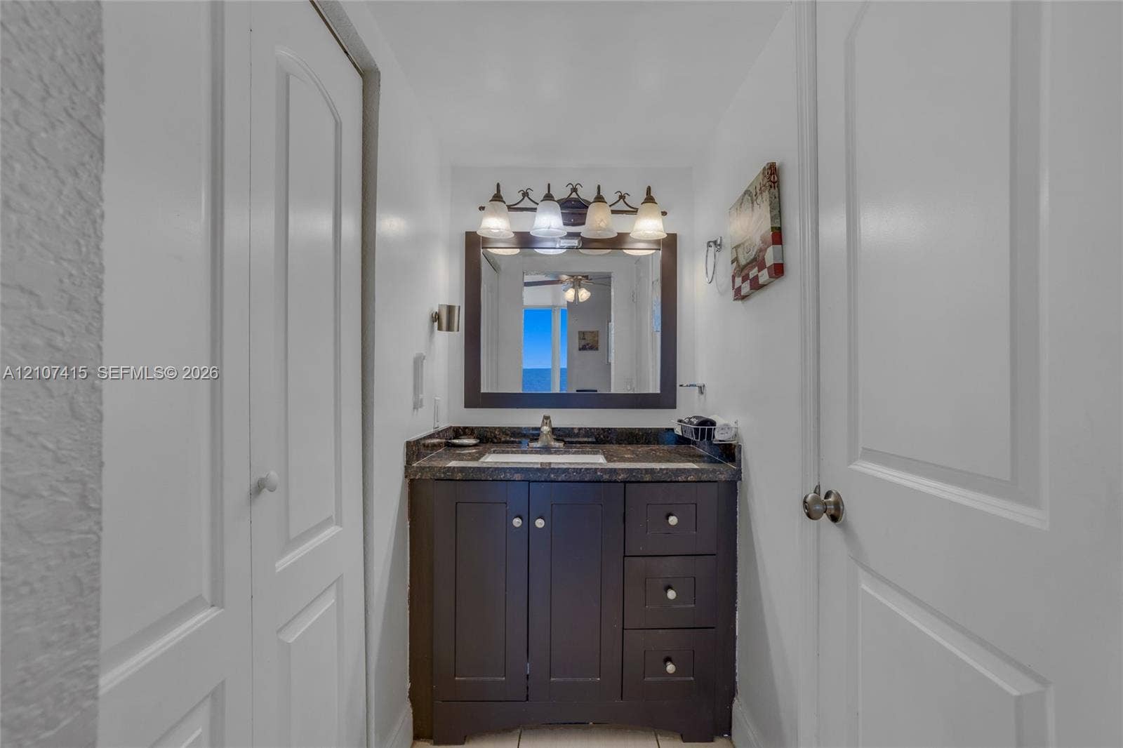 Dark cabinetry vanity featuring a stone countertop, an integrated rectangular sink, a framed mirror, and a multi-light fixture