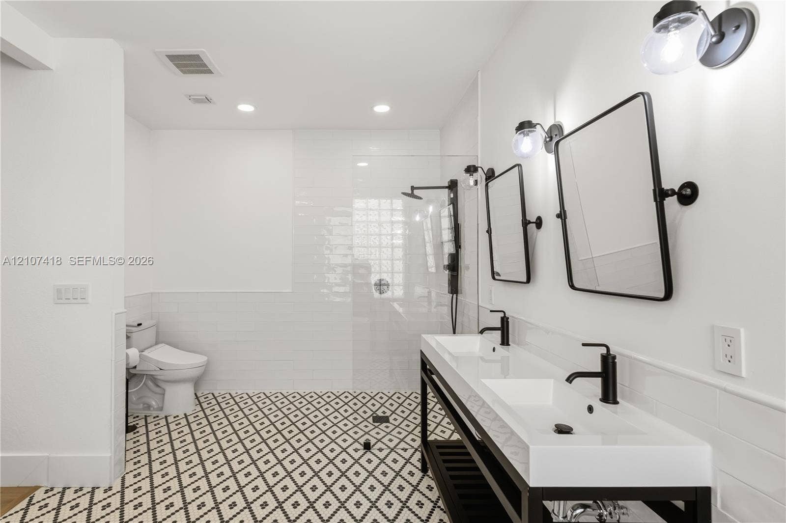 19305 Skyridge Circle, #n/a, Boca Raton, Boca Raton, FL 33498 Dual vanity with rectangular sinks, matte black fixtures, framed mirrors, glass-enclosed shower, and geometric patterned tile flooring
