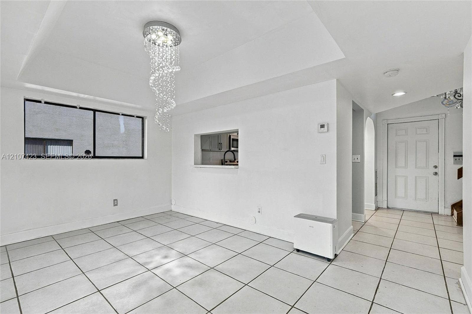 650 NE 195th Street, Miami, FL 33179 Open interior space featuring large-format ceramic tile flooring, a recessed ceiling with a crystal drop chandelier, and a cut-out wall opening