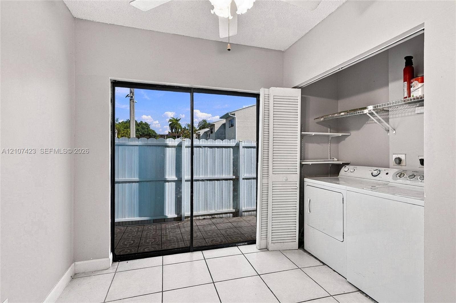650 NE 195th Street, Miami, FL 33179 Utility room featuring ceramic tile flooring, a ceiling fan, sliding glass door, and louvered closet doors with integrated wire shelving