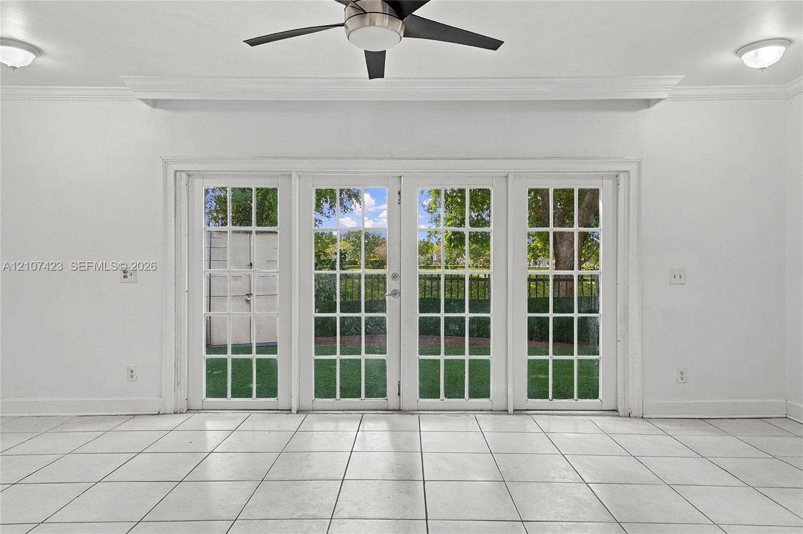 650 NE 195th Street, Miami, FL 33179 Set of four glass-paned French doors, neutral tile flooring, recessed and flush-mount ceiling lighting, and a multi-blade ceiling fan with integrated light