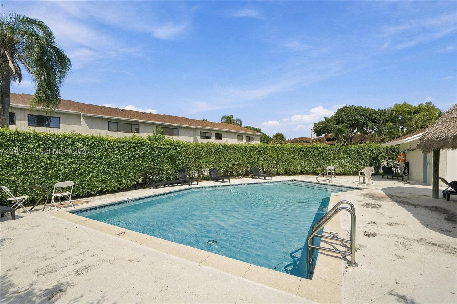 650 NE 195th Street, Miami, FL 33179 In-ground swimming pool featuring a metal ladder, concrete pool deck, and perimeter privacy hedges