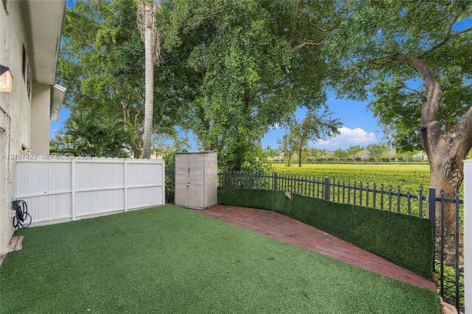 650 NE 195th Street, Miami, FL 33179 Backyard featuring synthetic turf, decorative brick-finish hardscaping, white vinyl perimeter fencing, and black metal perimeter railings
