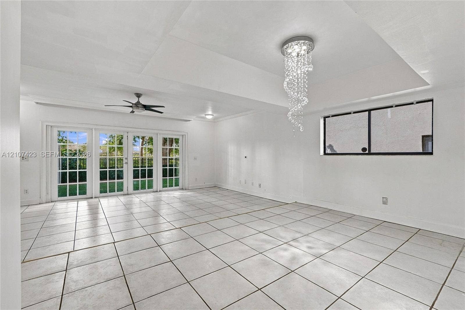 650 NE 195th Street, Miami, FL 33179 Interior space featuring tile flooring, a tray ceiling, crystal chandelier, ceiling fan, and multipane French doors