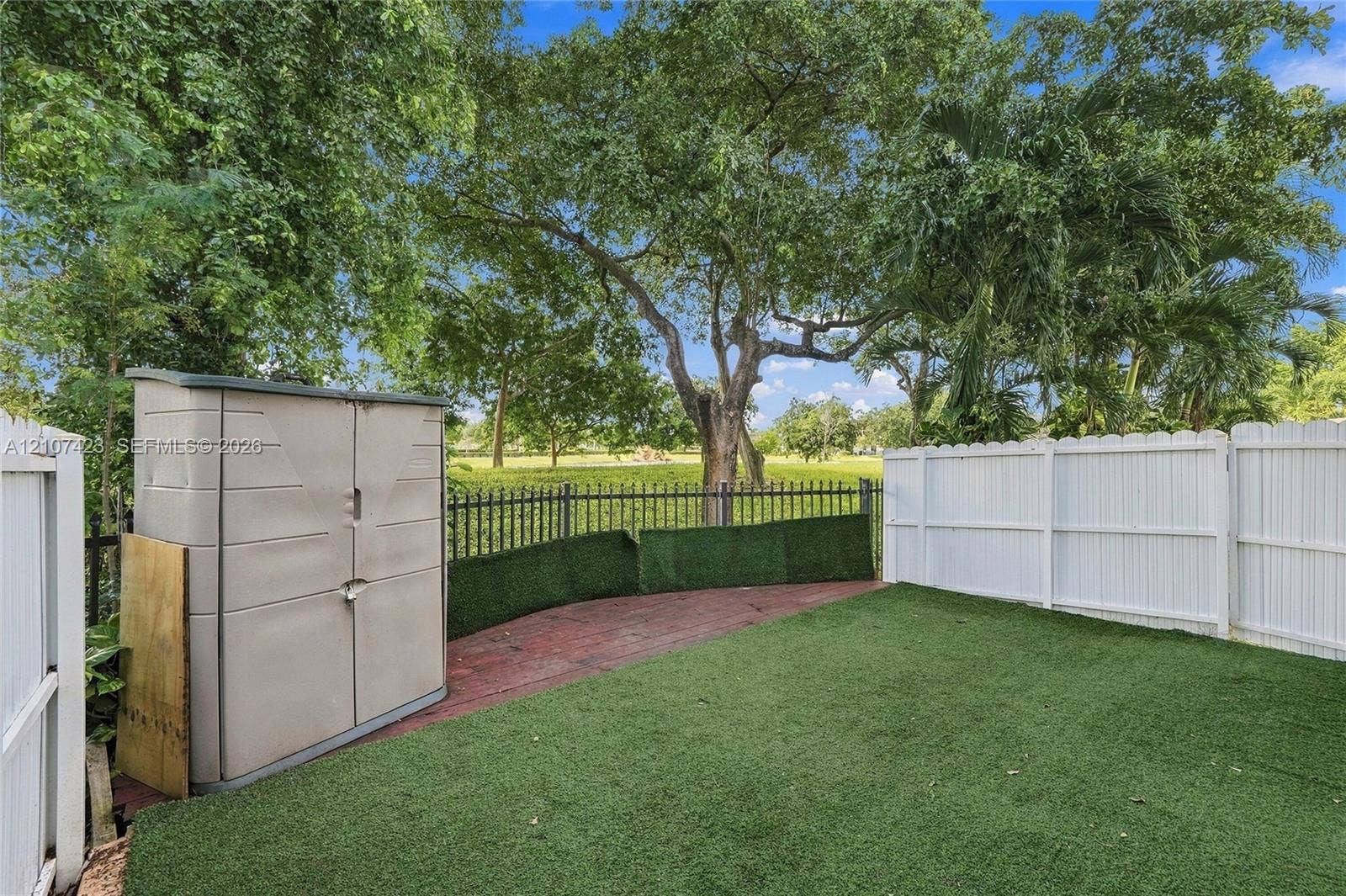 650 NE 195th Street, Miami, FL 33179 Backyard featuring synthetic turf, white vinyl privacy fencing, metal perimeter railing, and mature trees