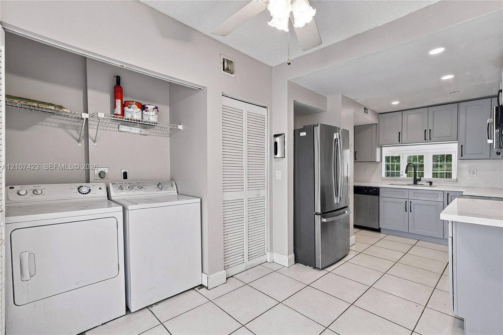 650 NE 195th Street, Miami, FL 33179 Kitchen and laundry area featuring grey cabinetry, stainless steel appliances, white tile flooring, louvered closet doors, and wire shelving