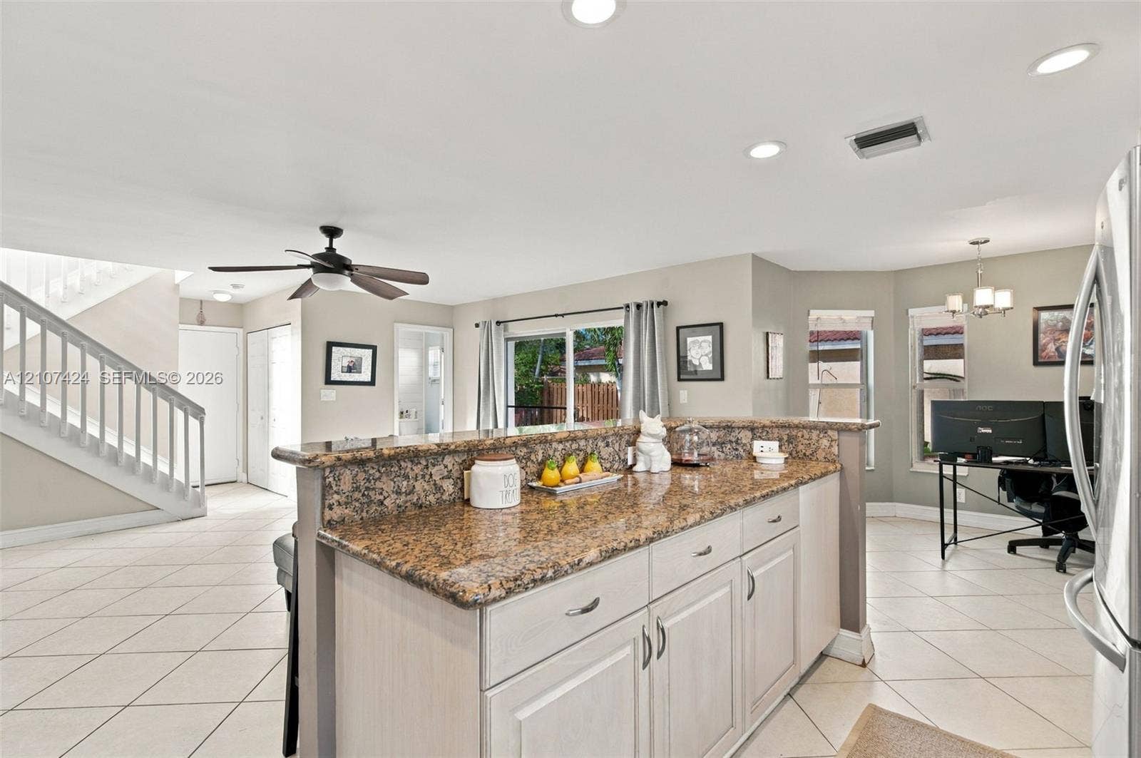 14702 Vista Luna Drive, Davie, FL 33325 Kitchen featuring a stone-topped island with shaker-style cabinetry, recessed lighting, neutral ceramic tile flooring, and a staircase with a wooden handrail