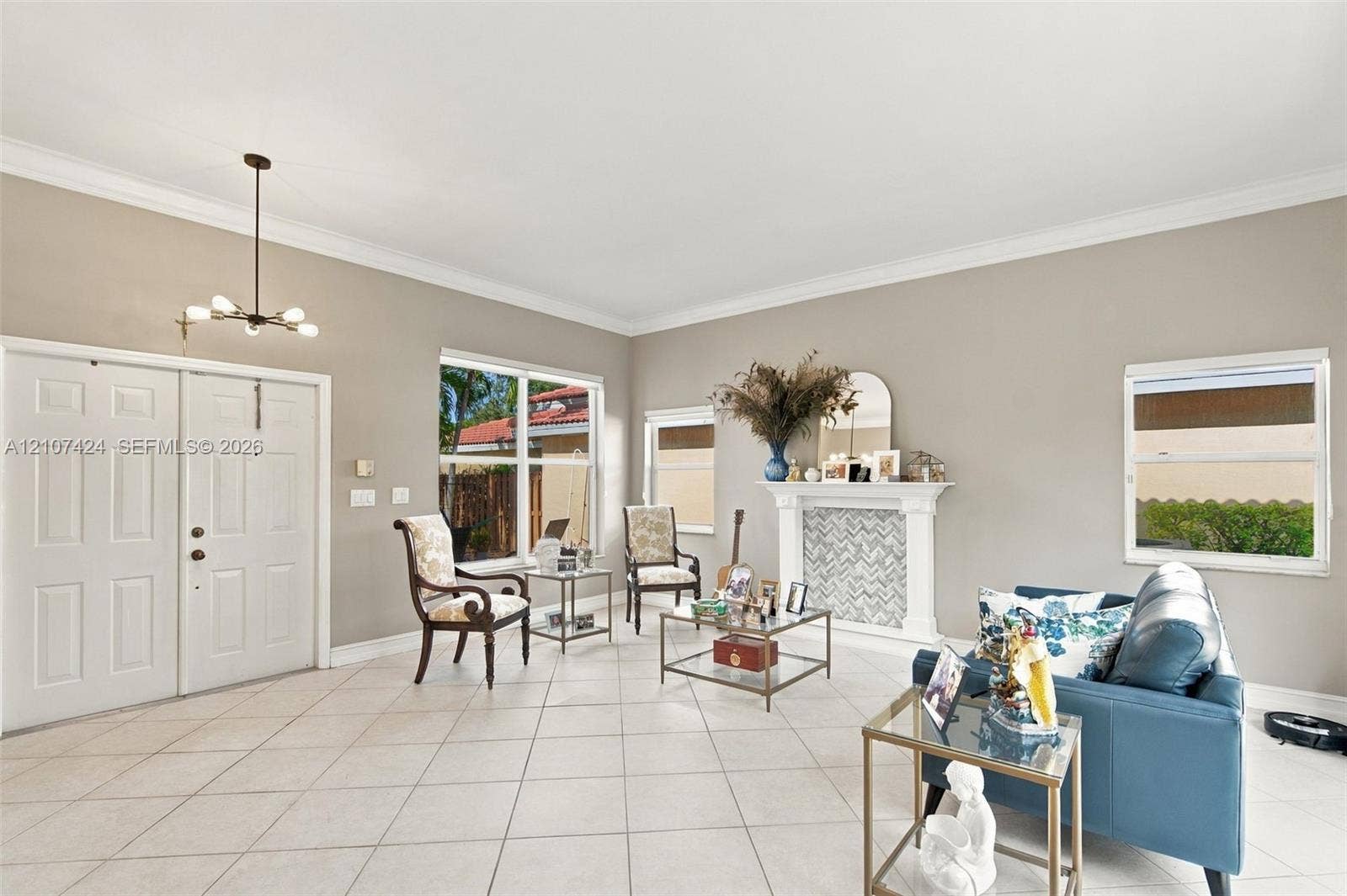 14702 Vista Luna Drive, Davie, FL 33325 Open living area featuring large-format diagonal tile flooring, crown molding, double-door entryway, decorative fireplace with mosaic tile surround, and multi-light chandelier