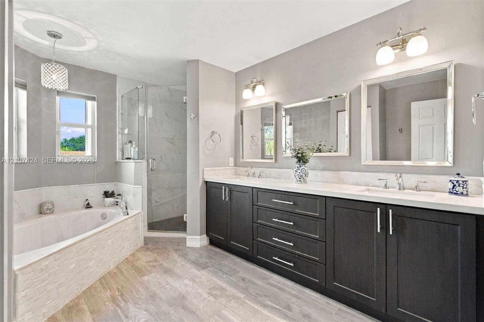 14702 Vista Luna Drive, Davie, FL 33325 Dual-sink vanity with dark cabinetry, light-toned countertop, and framed mirrors, featuring a separate soaking tub with stone-textured surround and a glass-enclosed shower with tiled interior