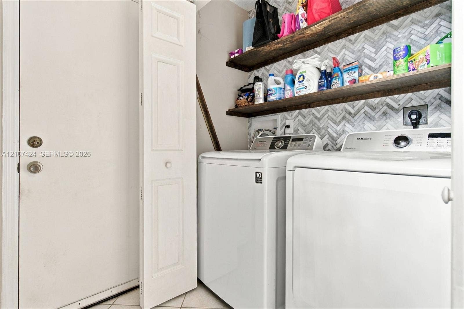 14702 Vista Luna Drive, Davie, FL 33325 Laundry space featuring herringbone-patterned wall tile, dual wood-finish floating shelves, and a bi-fold closet door on 1st floor