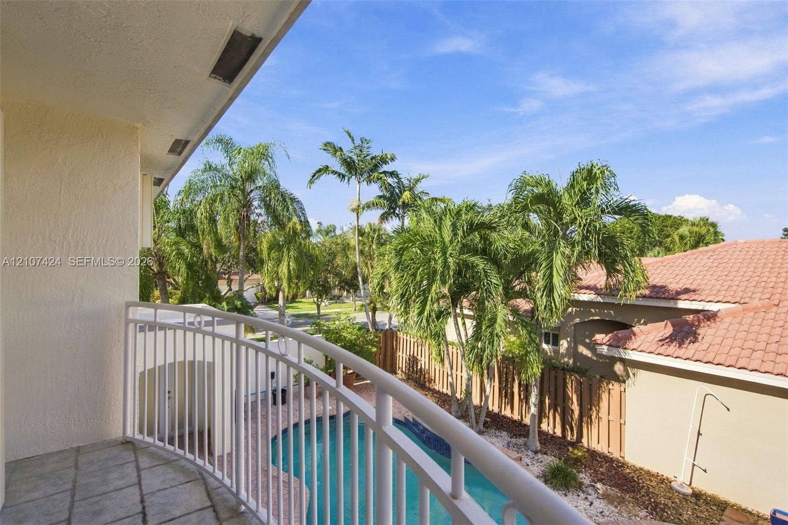 14702 Vista Luna Drive, Davie, FL 33325 Covered balcony featuring stone-tile flooring and a white metal railing overlooking a private pool, wood fencing, and mature palm trees