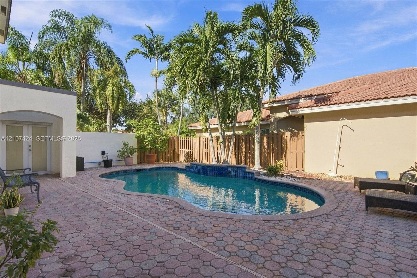 14702 Vista Luna Drive, Davie, FL 33325 Outdoor swimming pool featuring a decorative tile water feature, surrounded by extensive patterned paver hardscaping, mature palm trees, and full-height privacy fencing