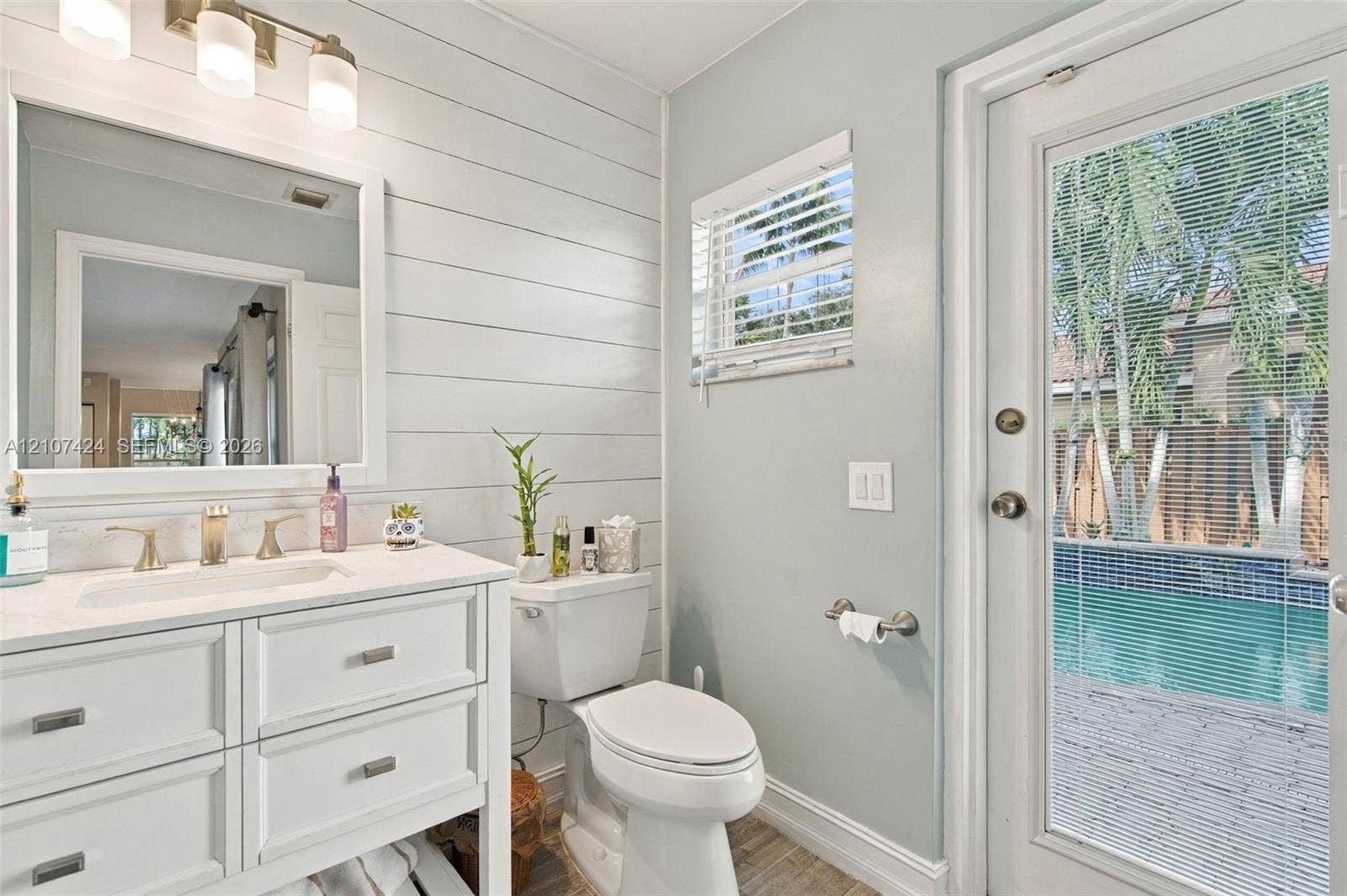 14702 Vista Luna Drive, Davie, FL 33325 Cabana 1/2 bathroom featuring shiplap wall detailing, a vanity with a light-toned countertop, a three-light fixture, and an exterior door with direct access to a pool area