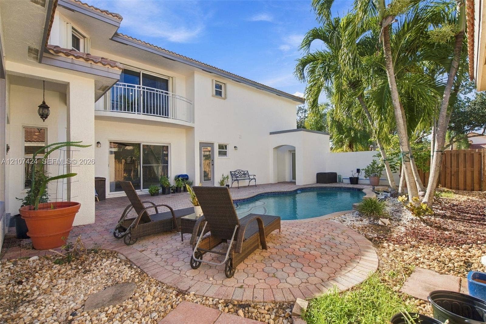 14702 Vista Luna Drive, Davie, FL 33325 Rear exterior featuring a stucco facade, second-story balcony with metal railings, in-ground pool, and a paved stone patio