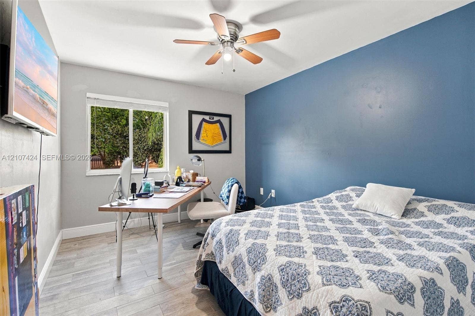 14702 Vista Luna Drive, Davie, FL 33325 Bedroom featuring wood-finish flooring, a neutral color palette with a blue accent wall, a sliding window, and a ceiling fan with integrated lighting