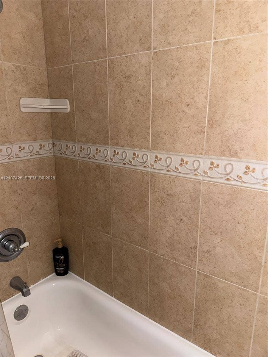 3475 N Country Club Drive, #704, Aventura, Aventura, FL 33180 Bathtub surround featuring neutral-toned square wall tiles, a decorative floral border inlay, integrated corner soap dish, and chrome-finish plumbing fixtures