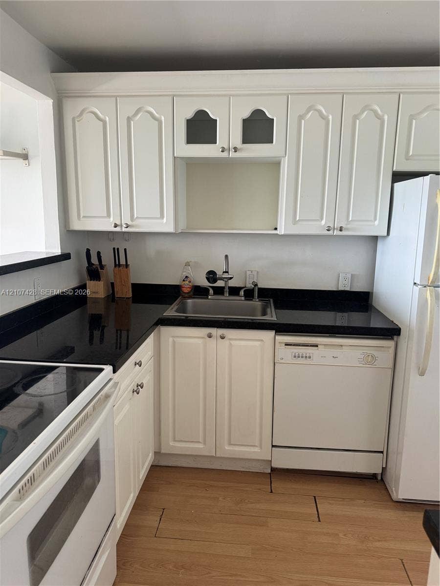 3475 N Country Club Drive, #704, Aventura, Aventura, FL 33180 Kitchen featuring white cabinetry with glass-panel accents, dark countertops, a stainless steel undermount sink, and wood-finish flooring
