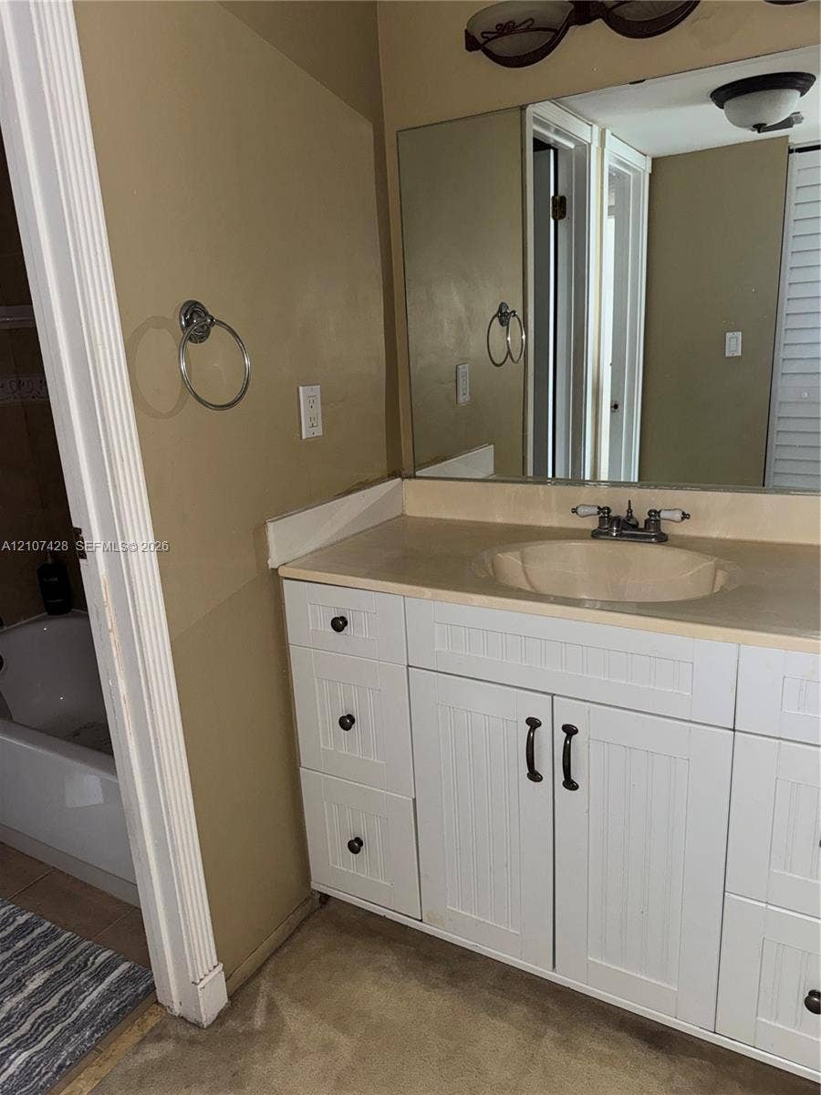 3475 N Country Club Drive, #704, Aventura, Aventura, FL 33180 White vanity with beadboard-style cabinetry, solid-surface countertop, integrated basin, chrome dual-handle faucet, and oversized wall-mounted mirror