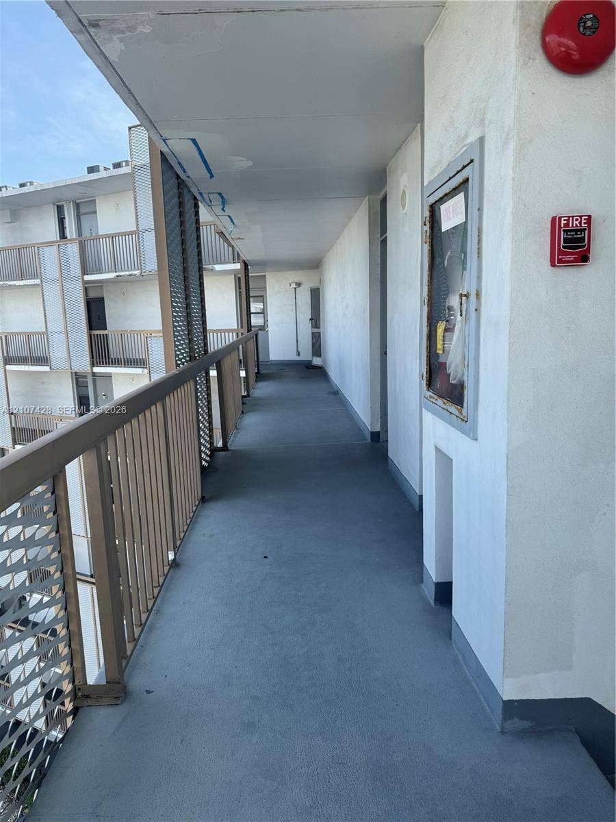 3475 N Country Club Drive, #704, Aventura, Aventura, FL 33180 Covered exterior walkway featuring a protective metal railing, textured stucco walls, and a recessed fire safety cabinet