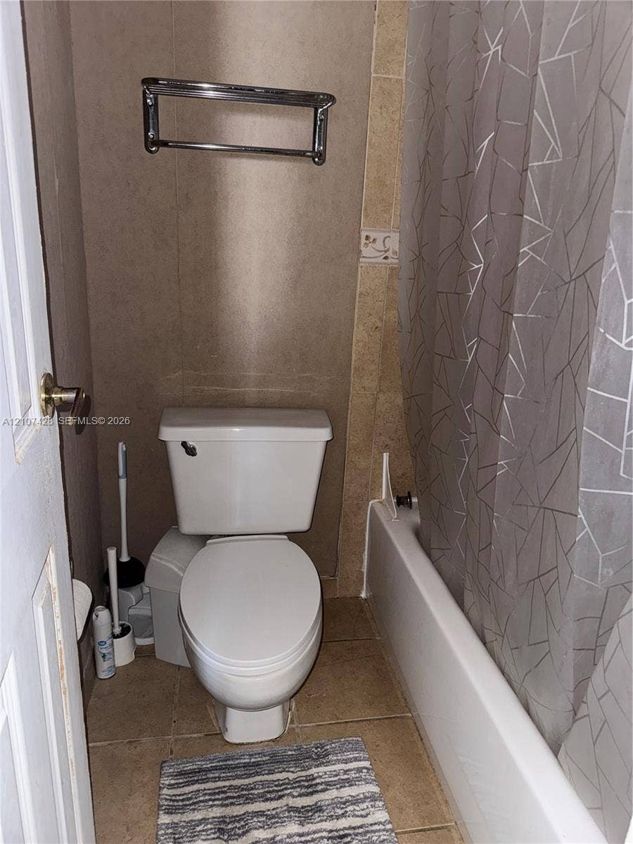 3475 N Country Club Drive, #704, Aventura, Aventura, FL 33180 Full bathroom featuring a white porcelain toilet, a standard-size soaking tub with a white surround, neutral-toned wall tiles, and a polished metal towel rack
