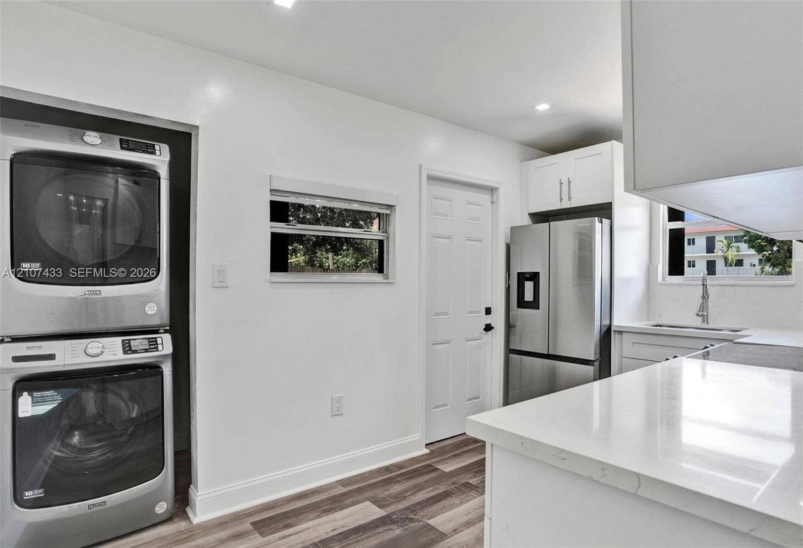 2135 SW 4th Street, Miami, FL 33135 Kitchen featuring stainless steel appliances, stacked laundry unit, white cabinetry, solid-surface countertops, and wood-finish flooring