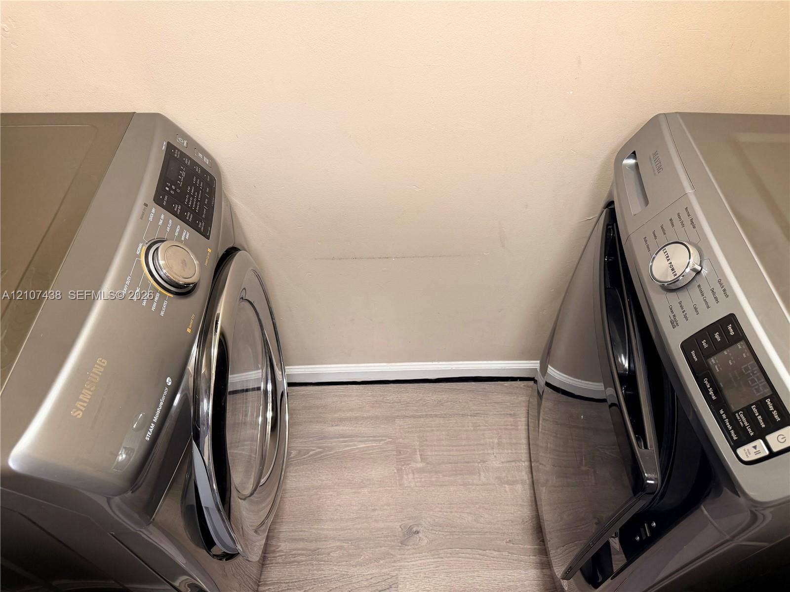 Laundry space featuring metallic-finish side-by-side Samsung appliances and wood-finish flooring