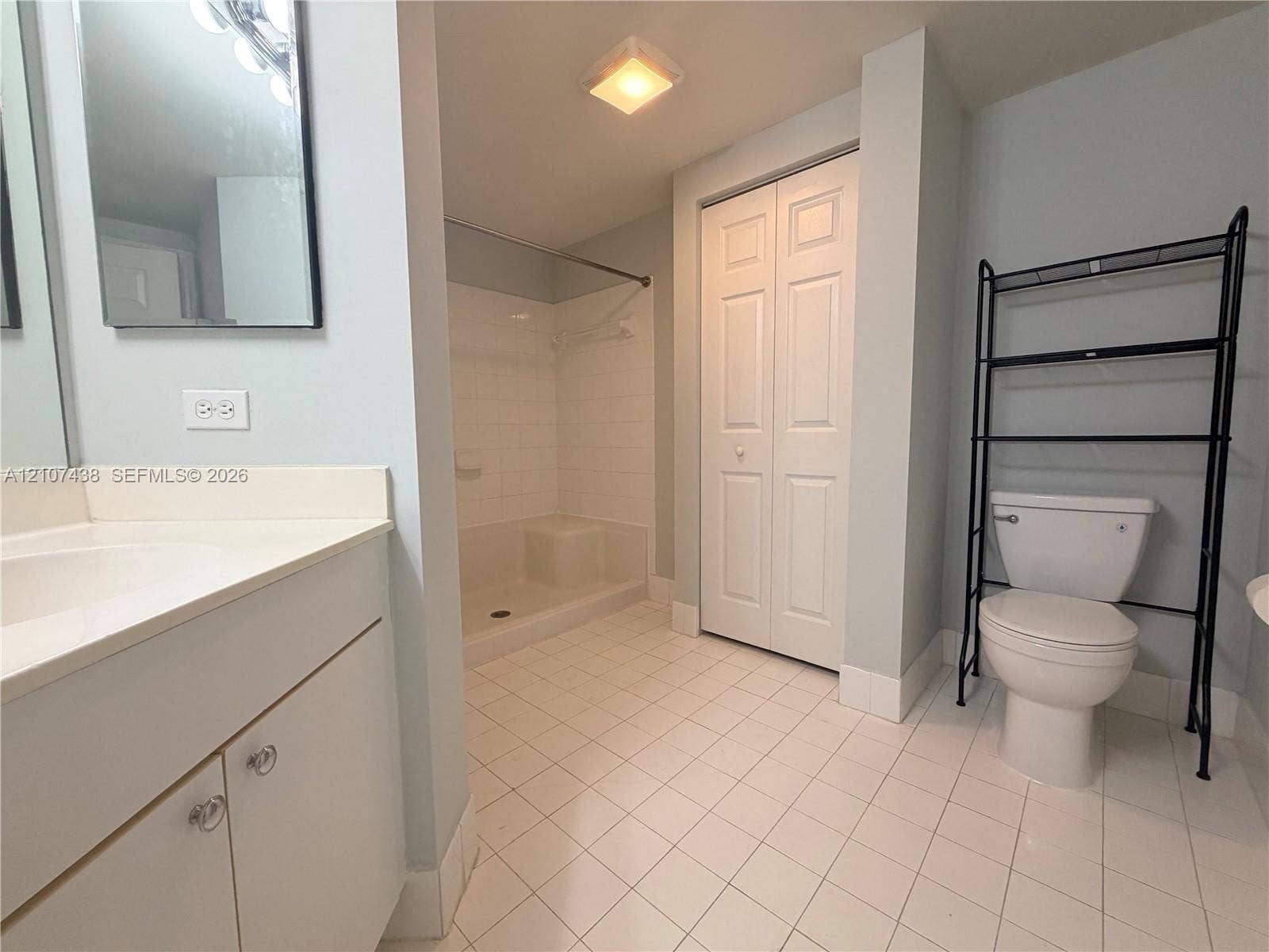 Bathroom featuring a white-finish vanity, a walk-in shower with tile surround, white floor tiling, and a bi-fold closet