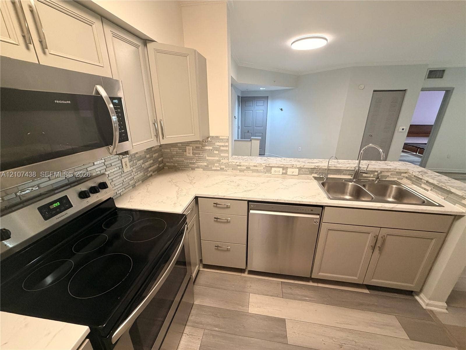 Kitchen featuring neutral-toned cabinetry, stainless steel appliances, patterned stone-style countertops, mosaic tile backsplash, and wood-finish flooring