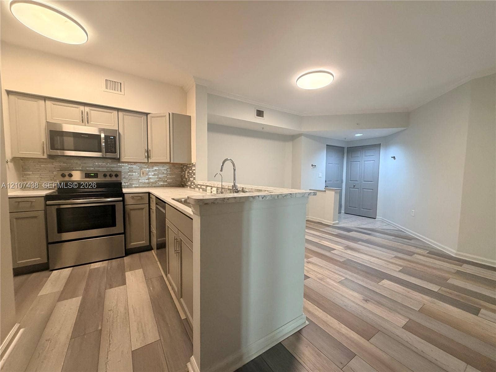Kitchen featuring neutral-toned cabinetry, stainless steel appliances, stone-finish countertops, tile backsplash, and wood-finish flooring
