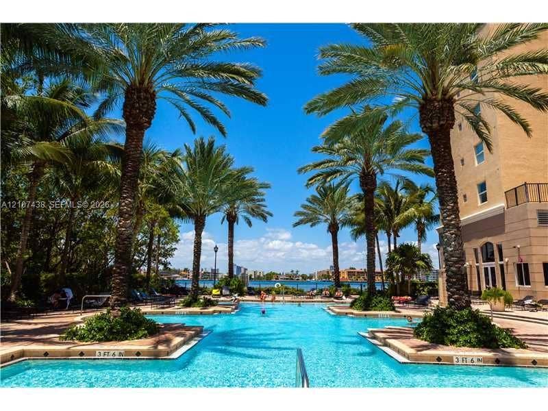 Swimming pool with paved surround, landscaped palm trees, and water frontage