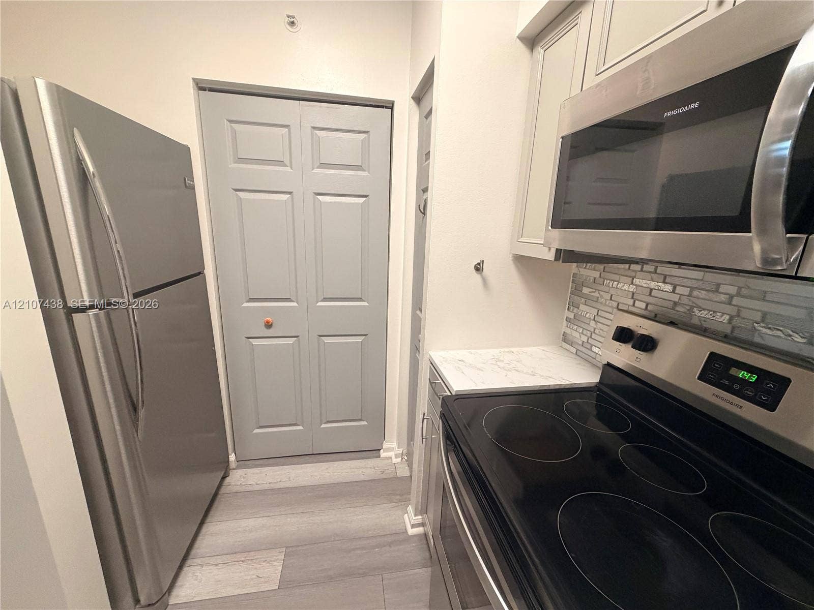 Stainless steel refrigerator, built-in microwave, flat-top electric range, stone-composite backsplash, and wood-finish flooring