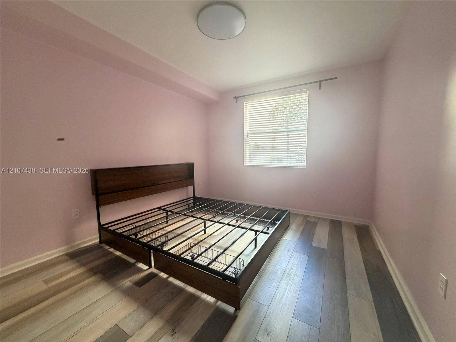 Room featuring wood-finish flooring, a neutral color palette, and a window with horizontal blinds