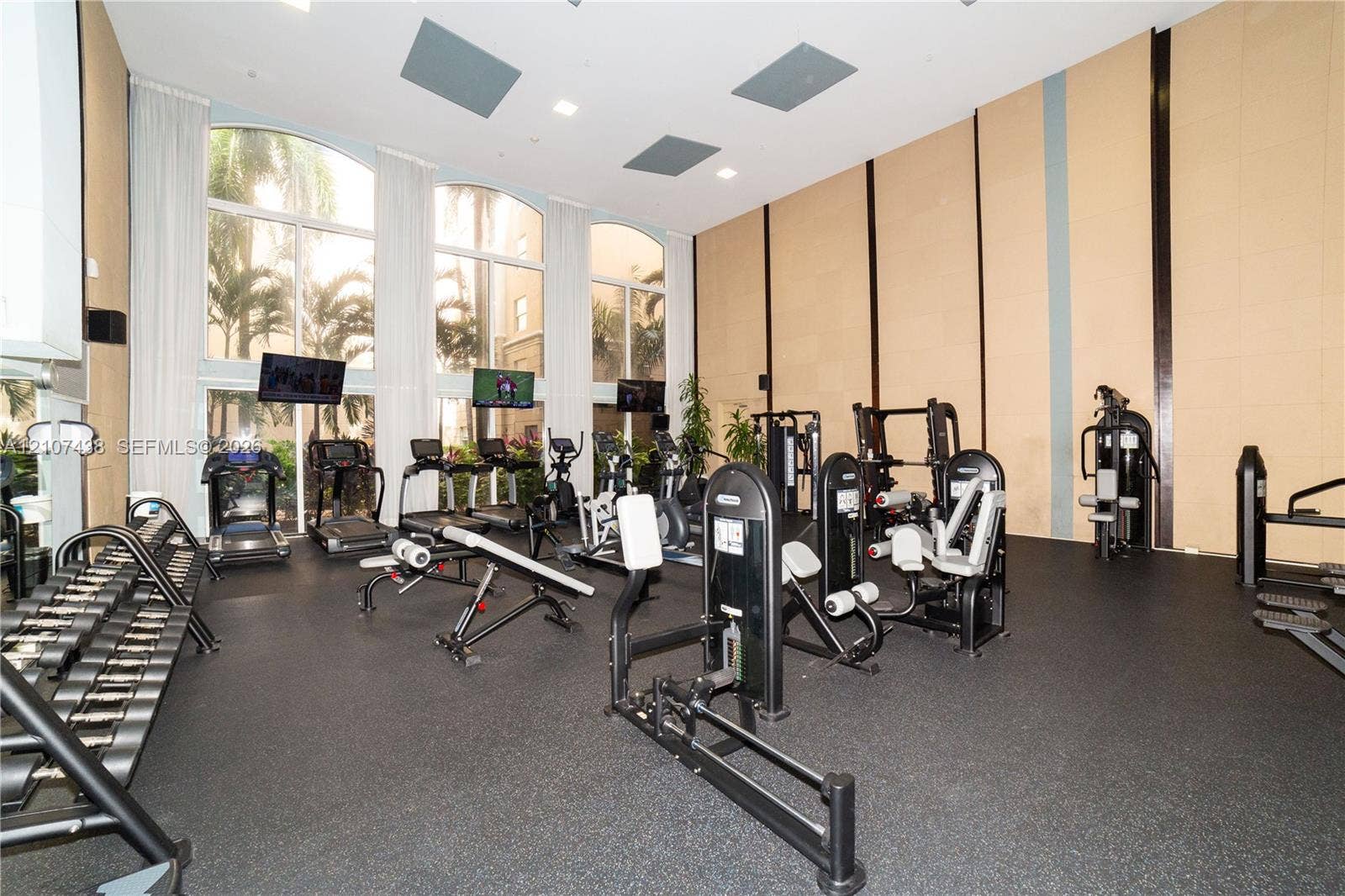 Fitness center featuring double-height ceilings, floor-to-ceiling arched windows, recessed lighting, and textured wall paneling