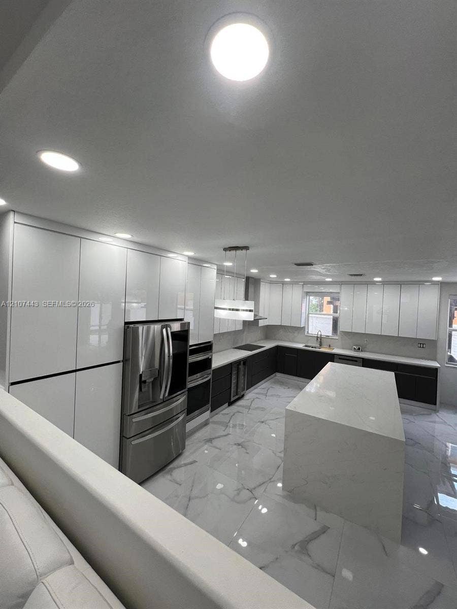 Kitchen featuring high-gloss cabinetry, large stone-surface island, stainless steel appliances, built-in dual ovens, and stone-finish flooring
