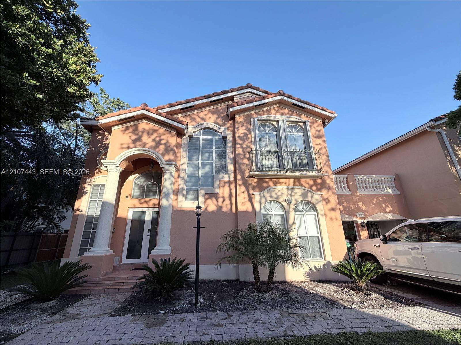 Two-story stucco exterior featuring a covered entryway with columns, arched window detailing, clay-tile roofline, and stone-paver walkway