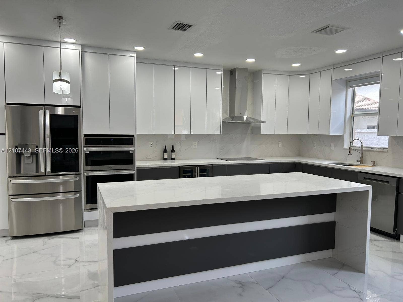 Kitchen featuring high-gloss white cabinetry, a center island with stone-finish countertops, stainless steel appliances, a chimney-style range hood, and large-format polished tile flooring