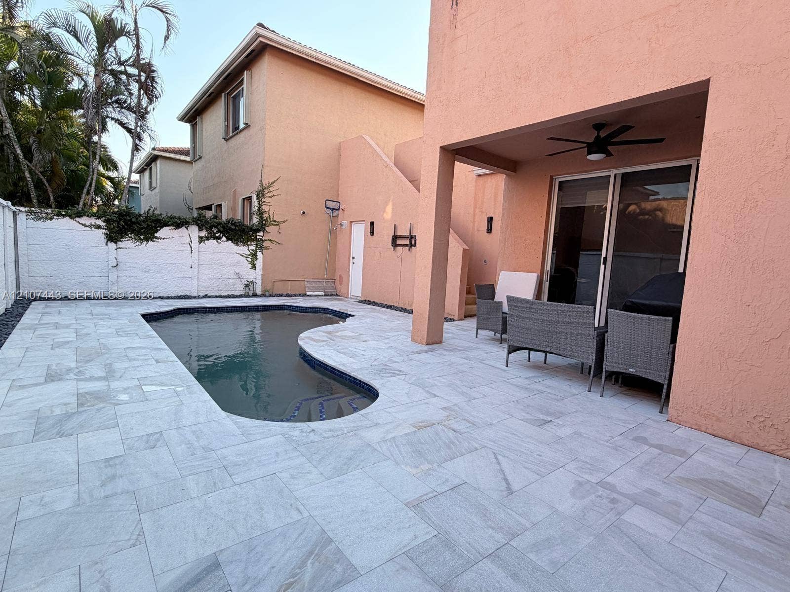 Stucco exterior featuring a covered patio, stone-tiled pool deck, in-ground swimming pool, and concrete perimeter wall