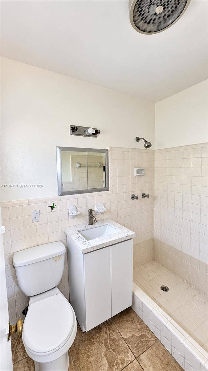 Bathroom featuring a white vanity with a stone-finish countertop, undermount sink, integrated shower with tile surround, and tile flooring
