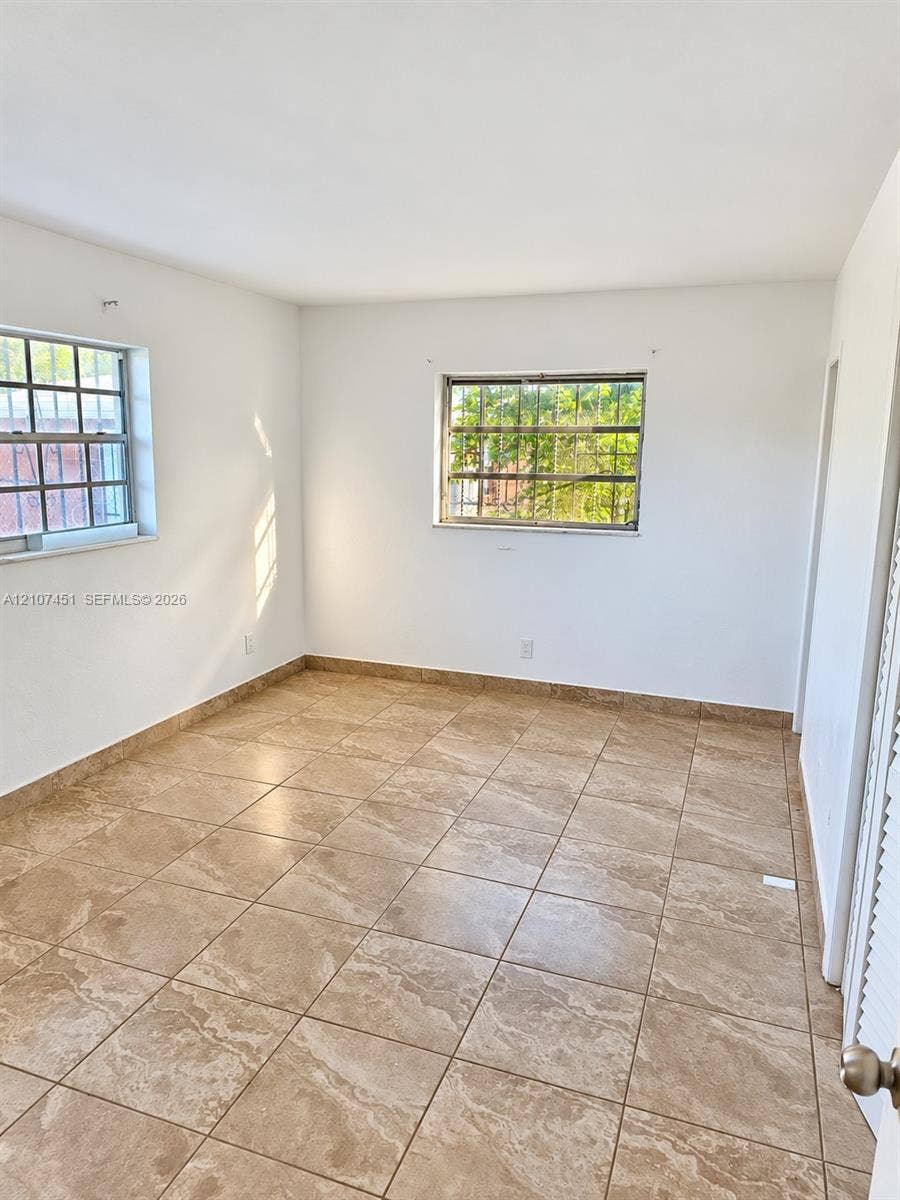 Interior space featuring neutral wall tones, large-format ceramic tile flooring, and dual windows with security bars