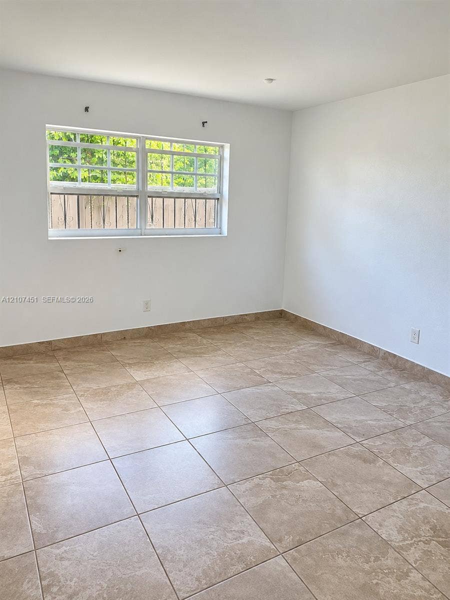 Interior room featuring large-format neutral tile flooring, expansive wall surfaces, and a multi-pane sliding window