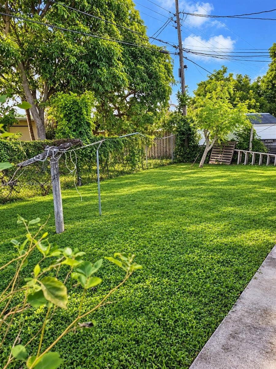 Backyard featuring a manicured lawn, perimeter chain-link fencing, and mature trees