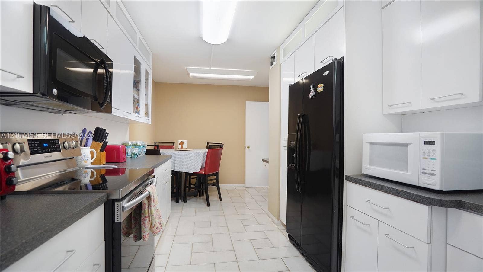 111 N Pompano Beach Boulevard, #304, Pompano Beach, FL 33062 Galley kitchen featuring white cabinetry, dark countertops, tile flooring, and integrated appliances