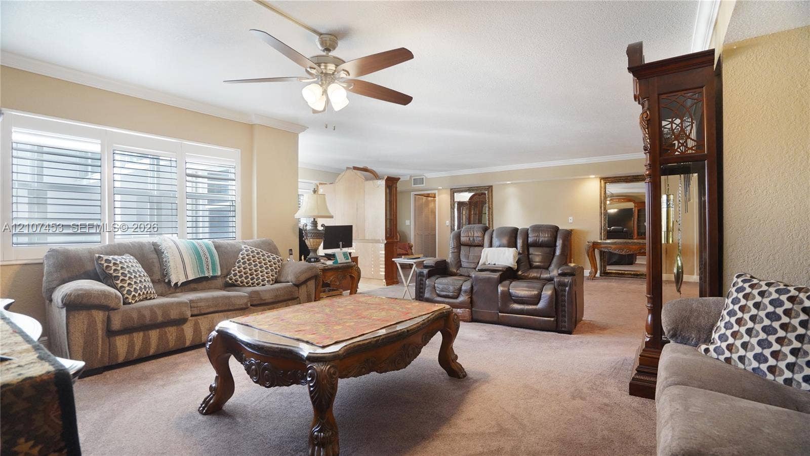 111 N Pompano Beach Boulevard, #304, Pompano Beach, FL 33062 Spacious living area featuring neutral wall tones, large window assembly with integrated shutters, and a ceiling-mounted fan with light fixture